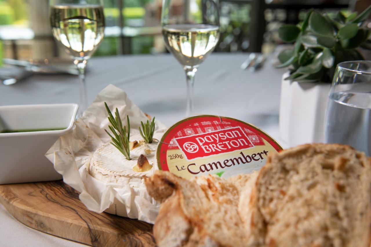 Macdonald Bath Spa Hotel Eksteriør bilde The photo features a dining setting that includes a wooden platter with a round Camembert cheese, garnished with fresh rosemary sprigs. Nearby, there is a serving of bread, likely sliced, and a small bowl, potentially for dipping or spreading. In the