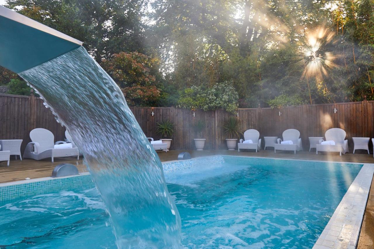 Macdonald Bath Spa Hotel Eksteriør bilde The photo shows a tranquil swimming pool surrounded by greenery. Water is cascading from a feature into the pool, creating a refreshing effect. In the background, there are white lounge chairs positioned neatly along the poolside, inviting relaxation