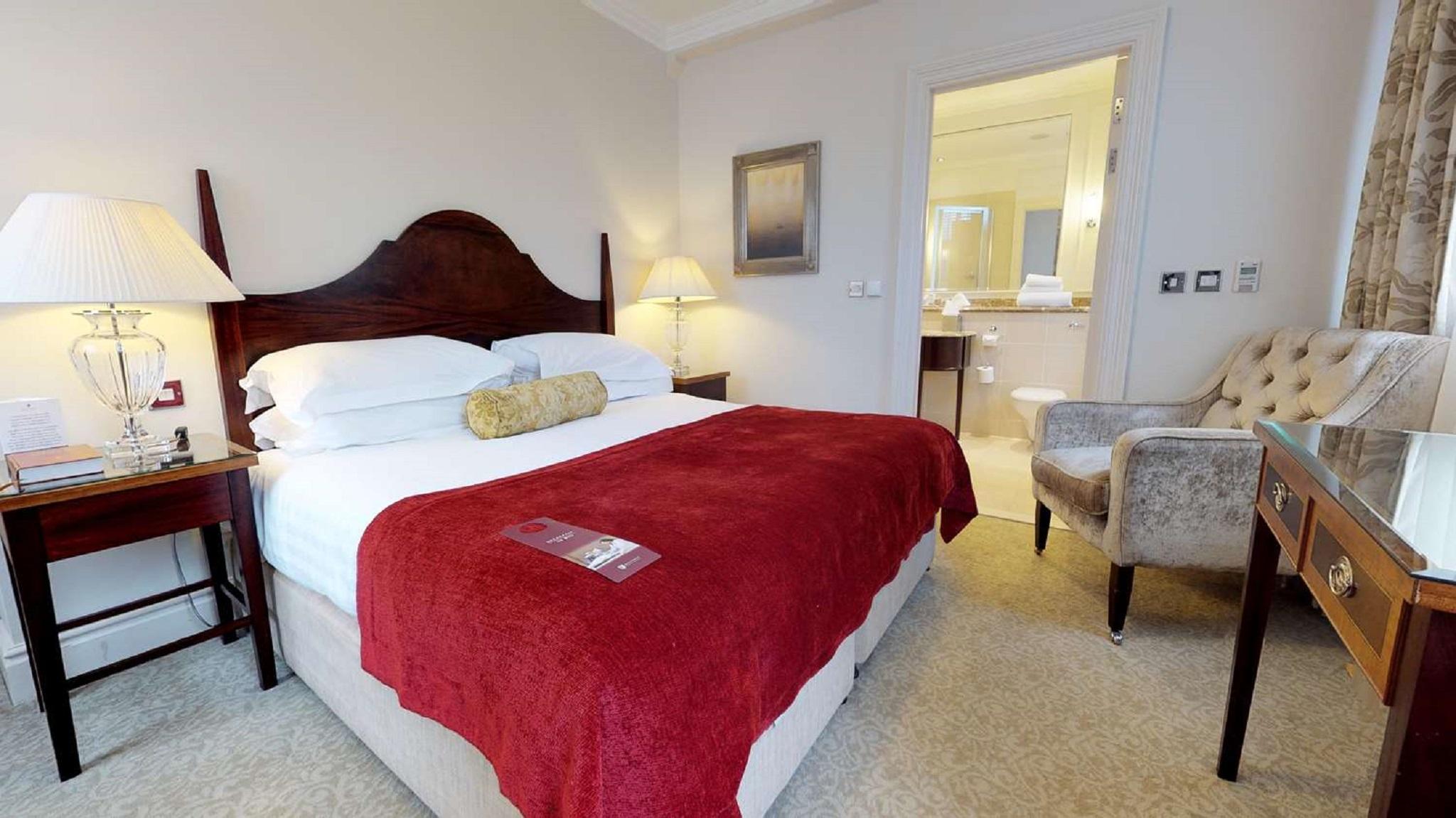 Macdonald Bath Spa Hotel Eksteriør bilde The photo shows a well-furnished hotel room. In the center, there is a large bed with white linens and a red throw blanket. A decorative pillow is placed on the bed. On either side of the bed, there are bedside tables with lamps. To the right, there 