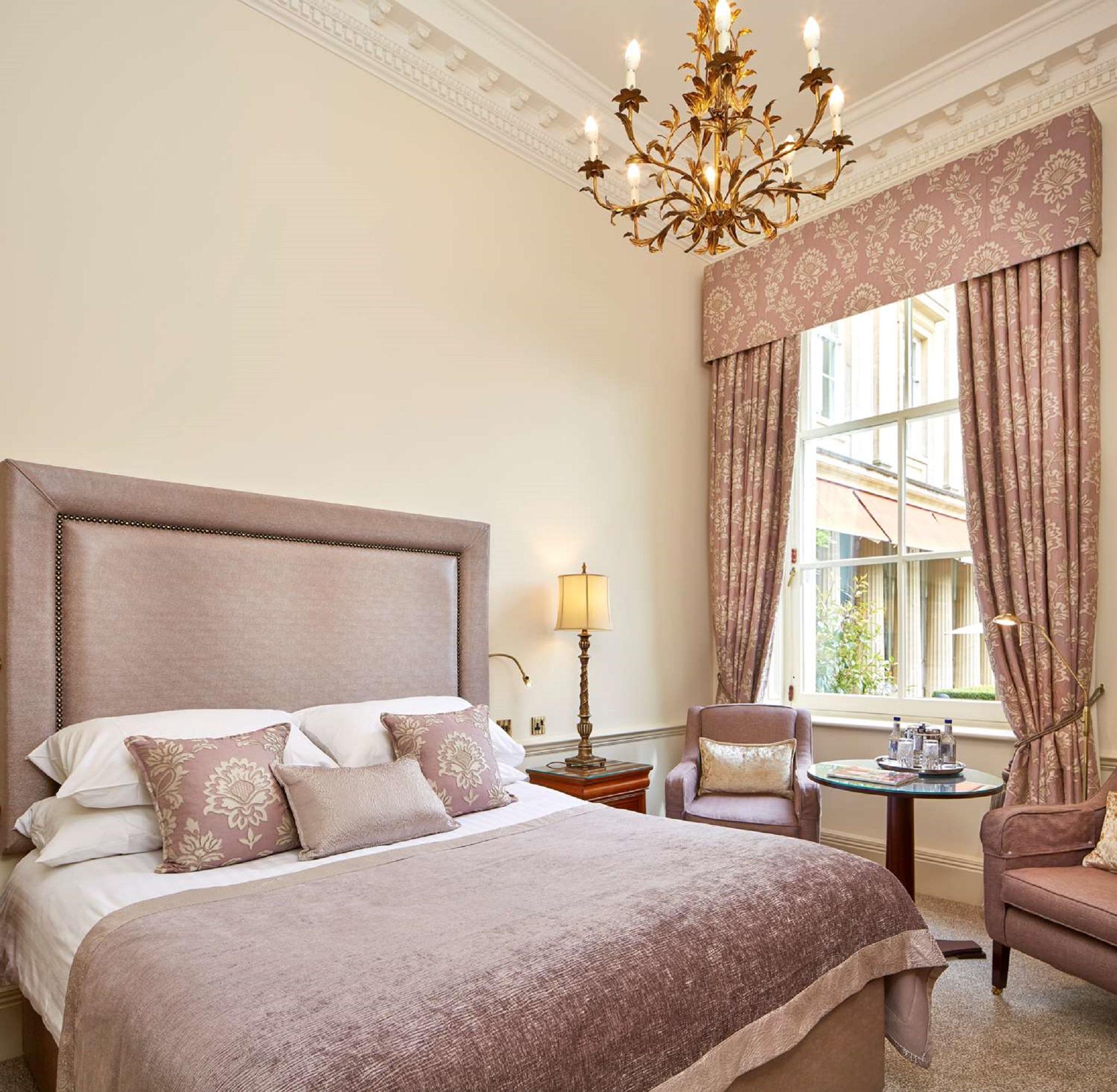 Macdonald Bath Spa Hotel Eksteriør bilde The photo shows a beautifully decorated hotel room. It features a large bed with a plush headboard, adorned with several decorative pillows. The walls are painted in a soft color, and there is a chandelier hanging from the ceiling. Natural light come
