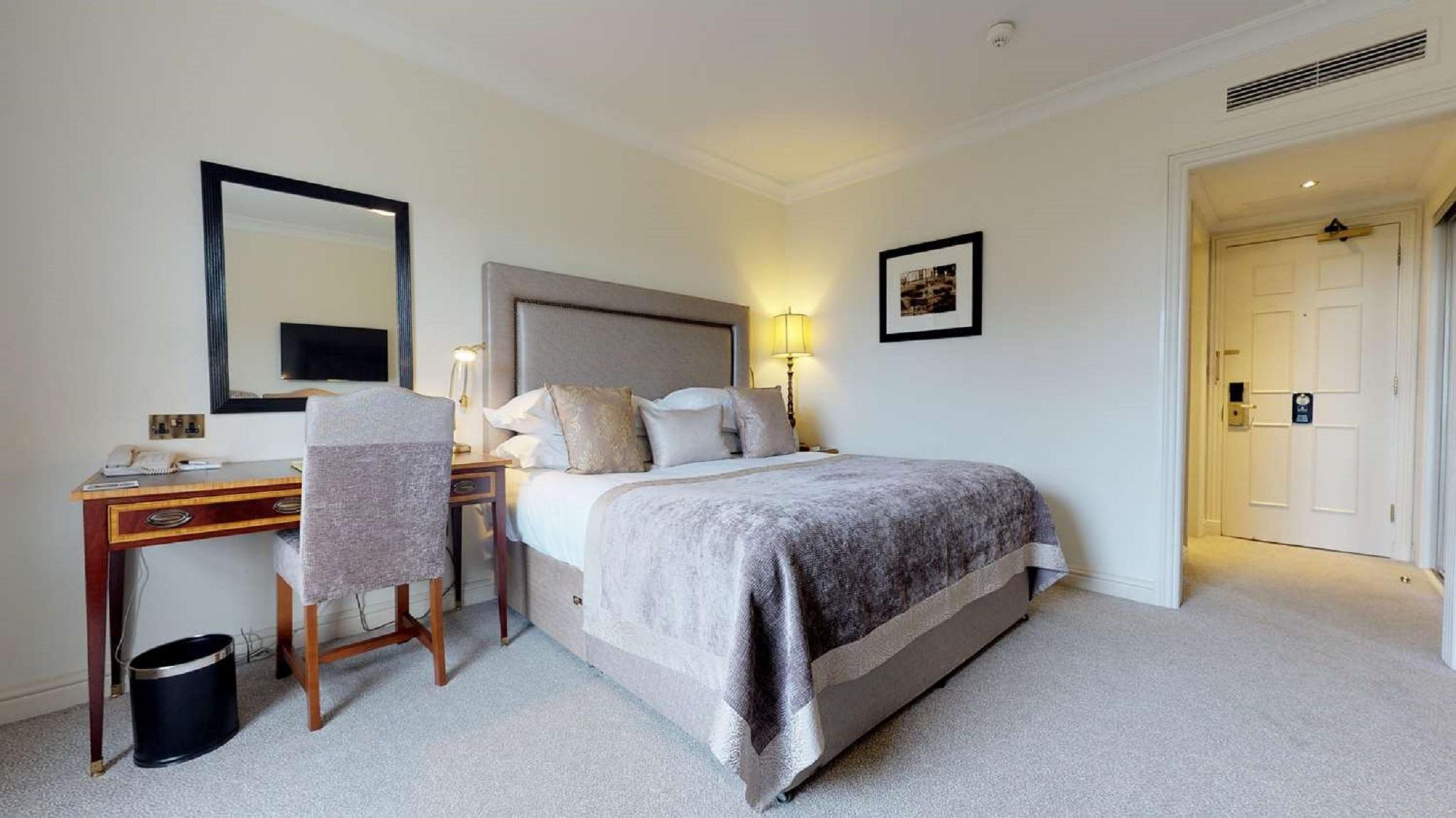 Macdonald Bath Spa Hotel Eksteriør bilde The photo shows a well-decorated hotel room. In the center, there's a comfortable bed with plush bedding and decorative pillows. A bedside table with a lamp is positioned next to the bed. To the left, there's a small desk with a chair, accompanied by