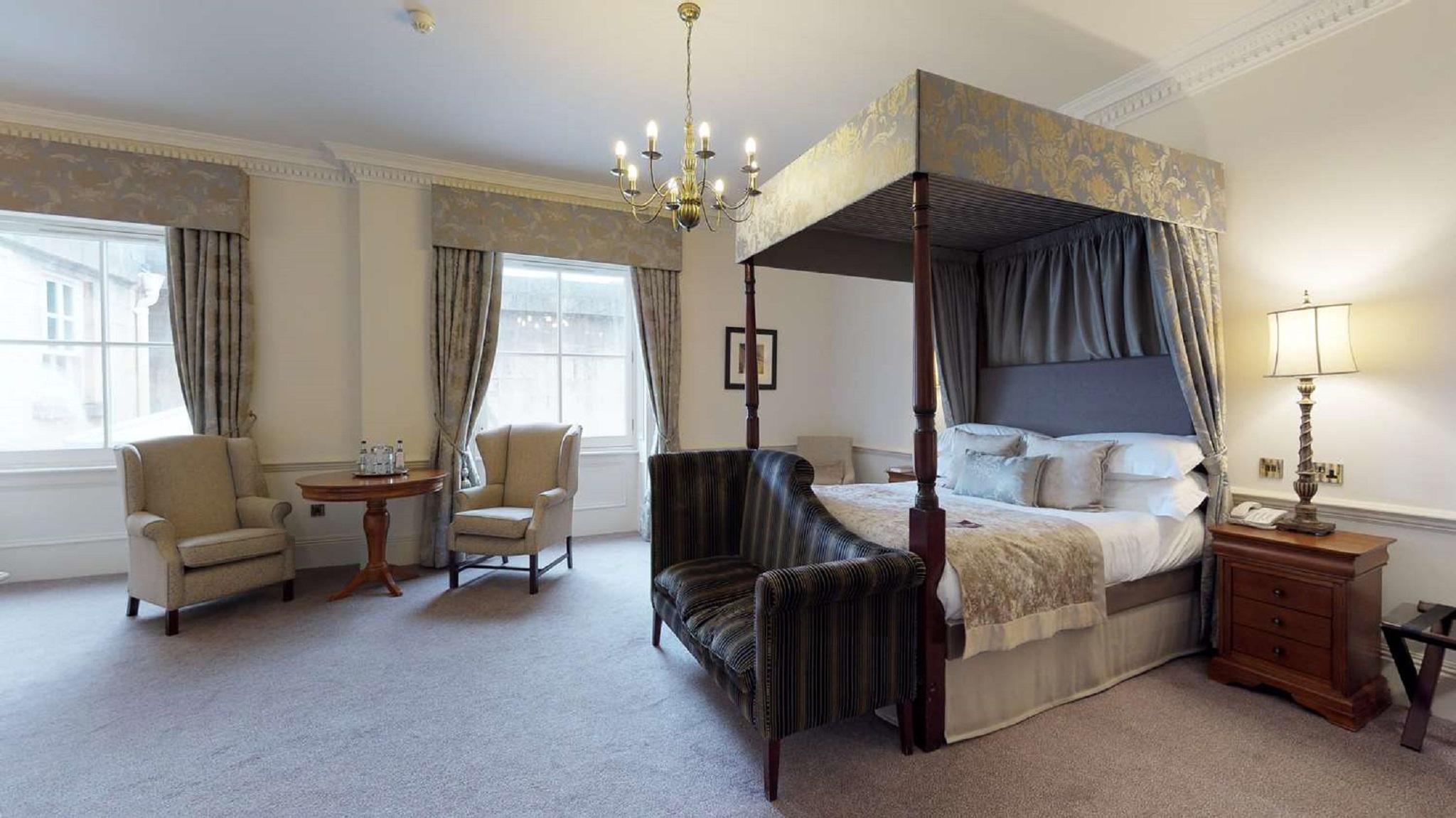 Macdonald Bath Spa Hotel Eksteriør bilde The photo shows a stylish hotel room featuring a four-poster bed with a decorative canopy. The bed is positioned prominently in the center, surrounded by plush bedding. To the side, there are two armchairs with a small round table between them, creat