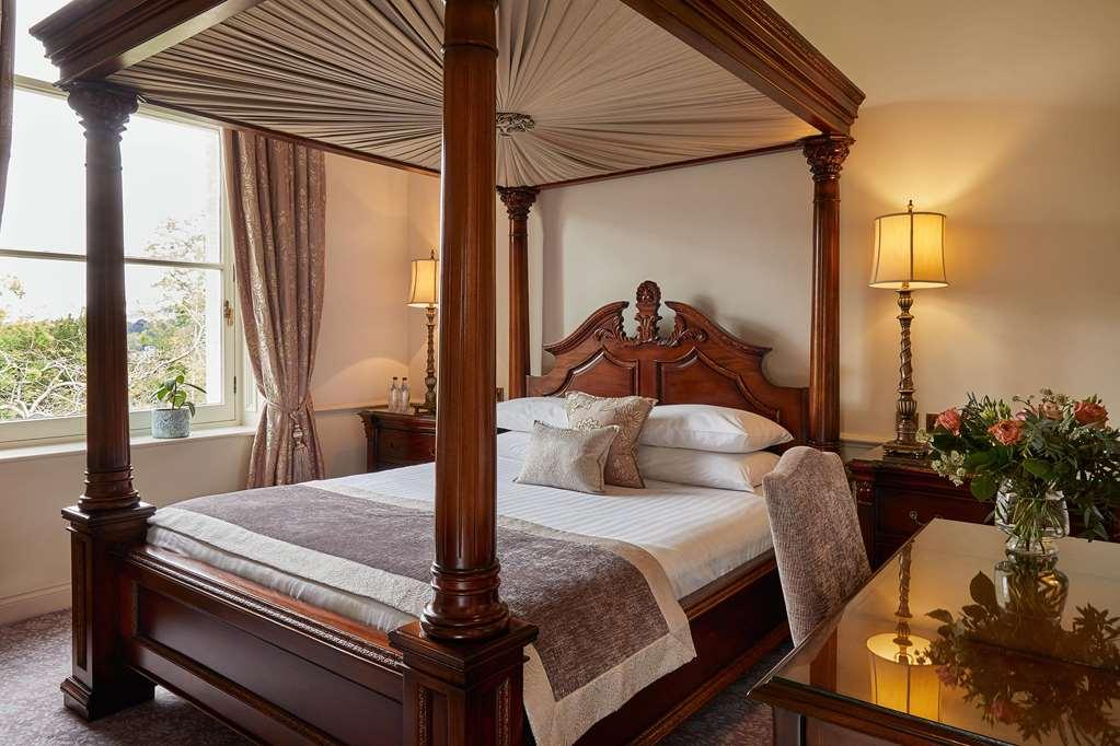 Macdonald Bath Spa Hotel Rom bilde The photo shows a beautifully designed bedroom featuring a four-poster bed made of dark wood. The bed has an elaborately carved headboard and is adorned with a light-colored bedding set. Above the bed, there is a canopy that adds an elegant touch. On