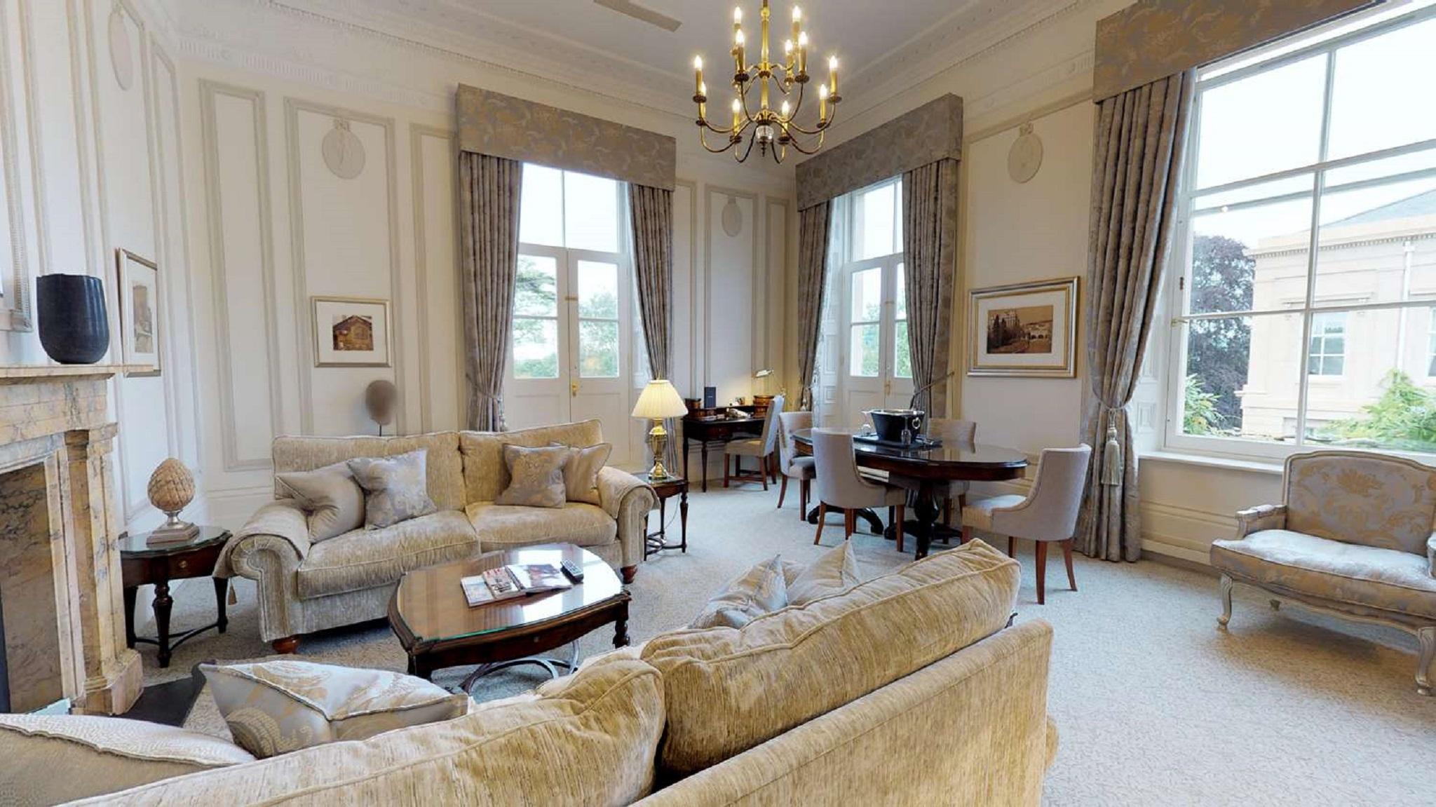 Macdonald Bath Spa Hotel Eksteriør bilde The photo displays a spacious and elegantly furnished living room. It features plush sofas and armchairs arranged around a central coffee table, creating a cozy seating area. Large windows adorned with long curtains allow natural light to fill the ro