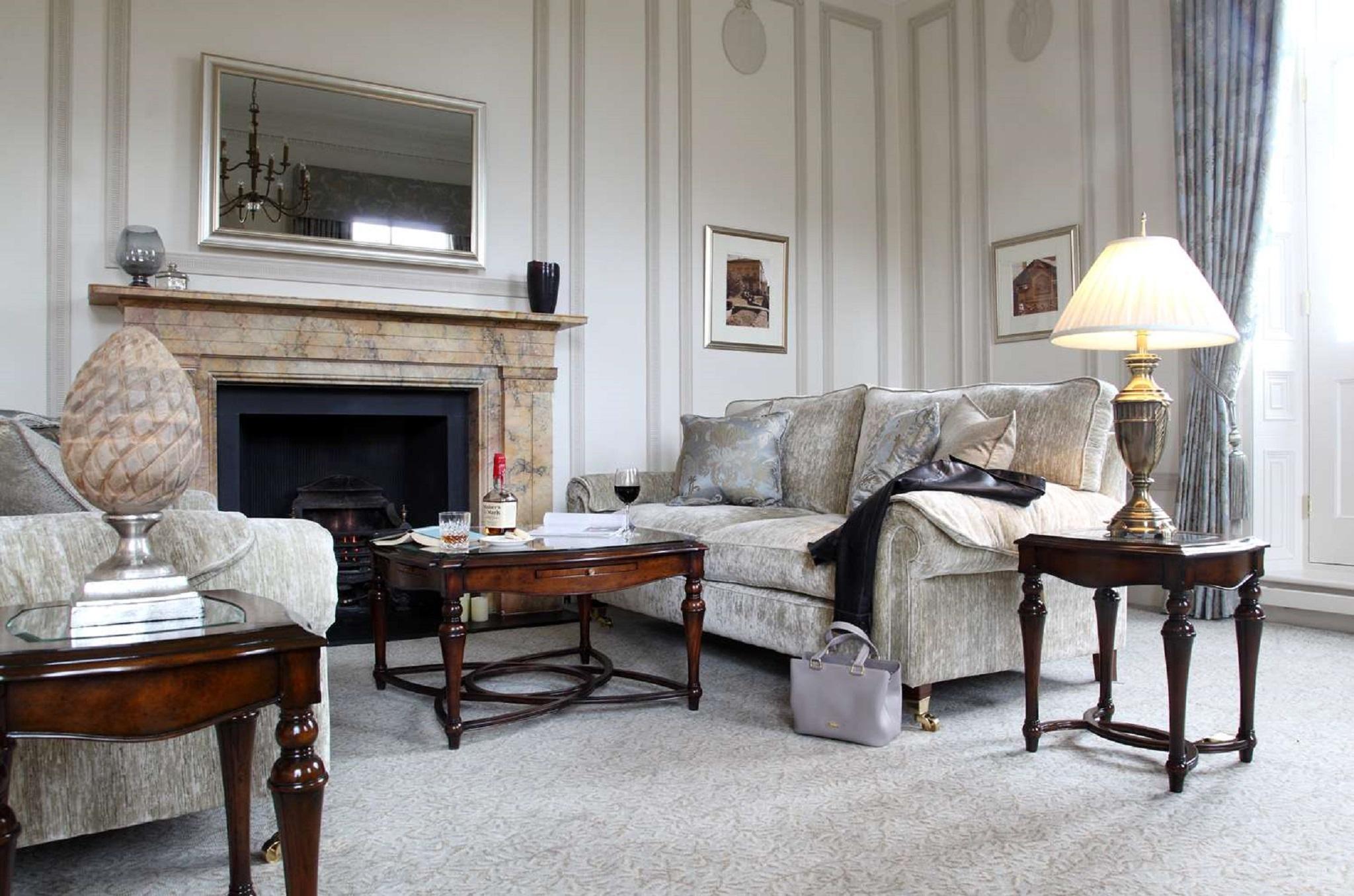 Macdonald Bath Spa Hotel Eksteriør bilde The photo shows a stylish living room. It features a plush light-colored sofa adorned with decorative pillows. Next to the sofa, there is a small wooden coffee table with a decorative item and a bottle of wine, along with a glass. A larger wooden tab