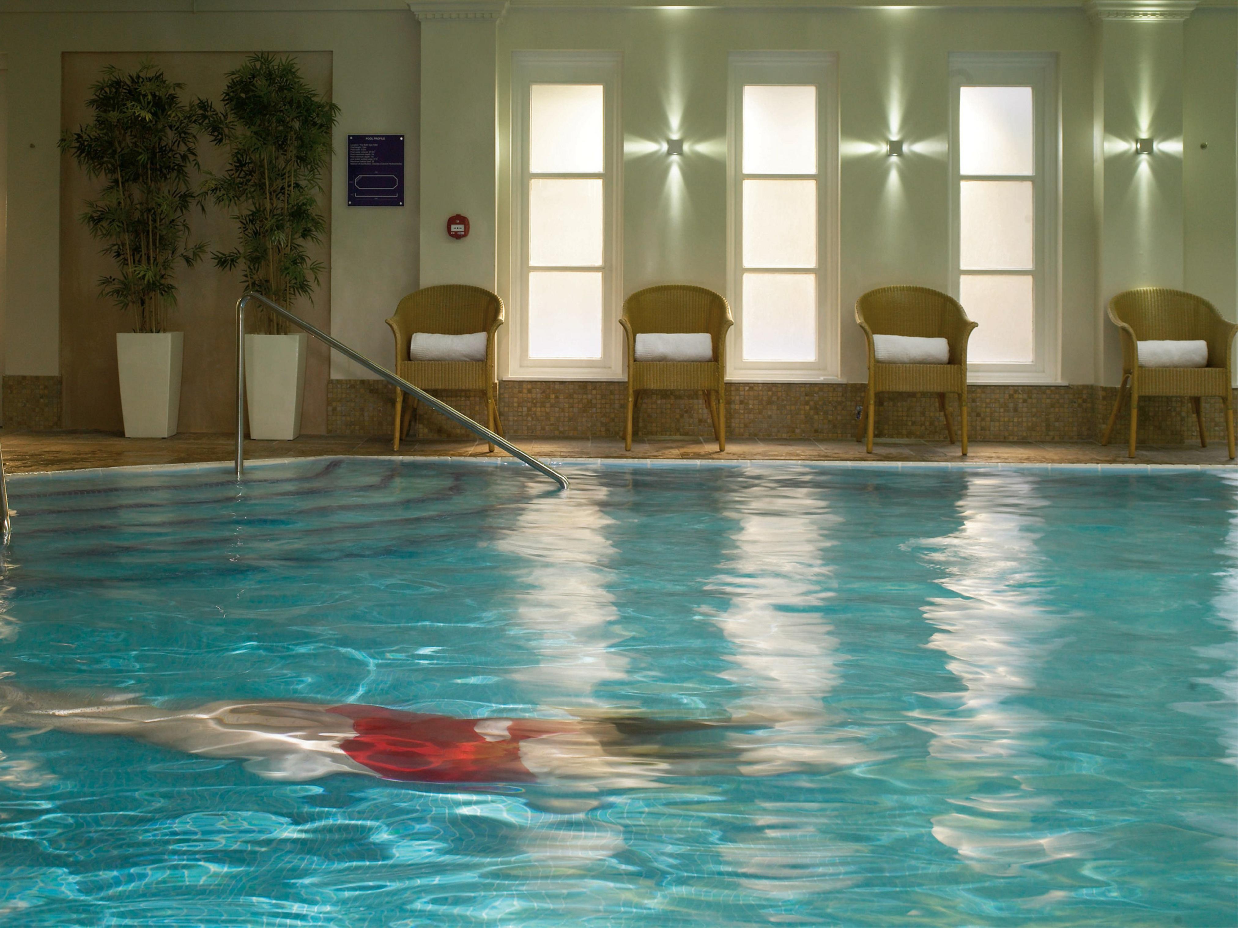 Macdonald Bath Spa Hotel Eksteriør bilde The photo shows an indoor swimming pool with clear, blue water. In the pool, a person is swimming, partially submerged, and wearing a red swimsuit. Surrounding the pool, there are several empty chairs arranged along the side, along with potted plants