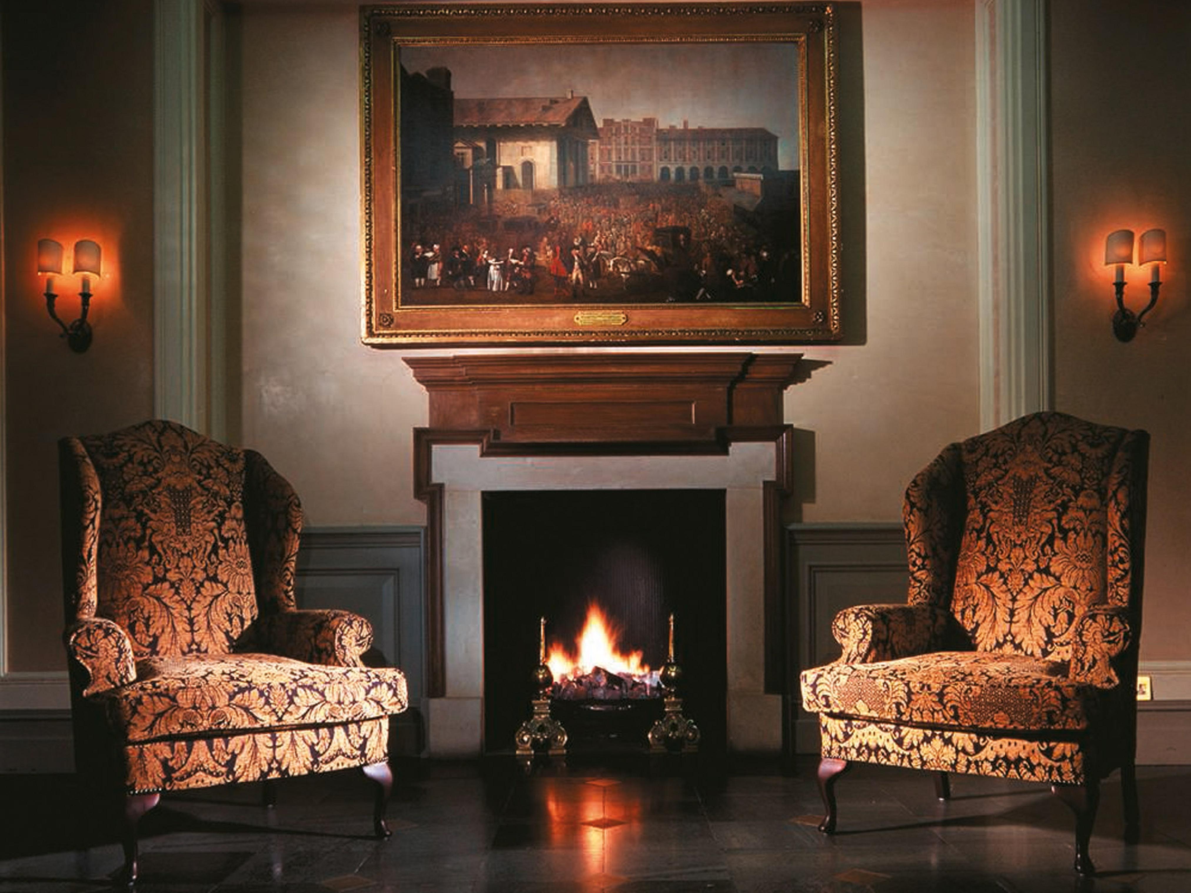 Macdonald Bath Spa Hotel Eksteriør bilde The image shows a cozy indoor setting featuring two ornate armchairs placed opposite a fireplace. Above the fireplace hangs a large painting in a decorative frame. The warm glow from the fire illuminates the room, and there are wall sconces providing