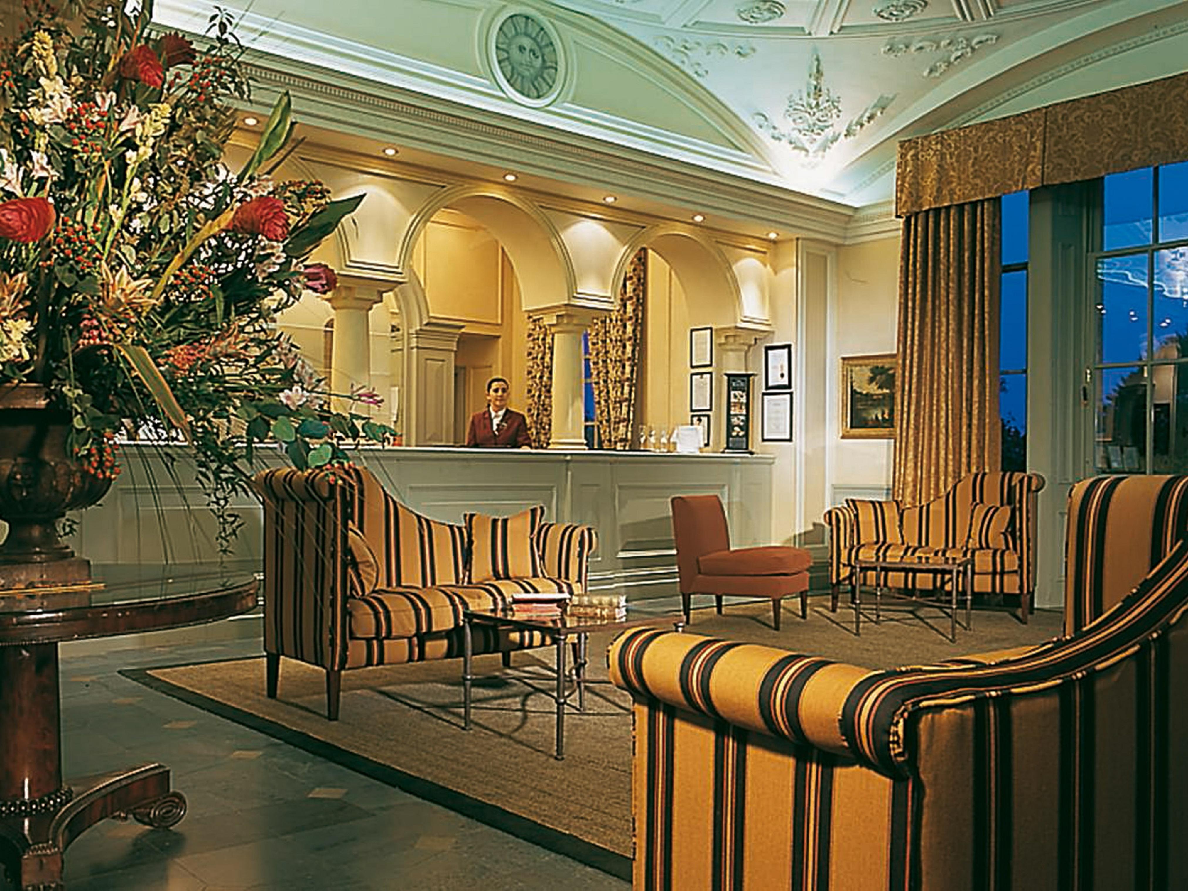 Macdonald Bath Spa Hotel Eksteriør bilde The photo shows an elegant hotel lobby. The area features a reception desk with a staff member behind it. Surrounding the reception are comfortable seating arrangements, including striped armchairs and a brown chair. A large vase with an elaborate fl