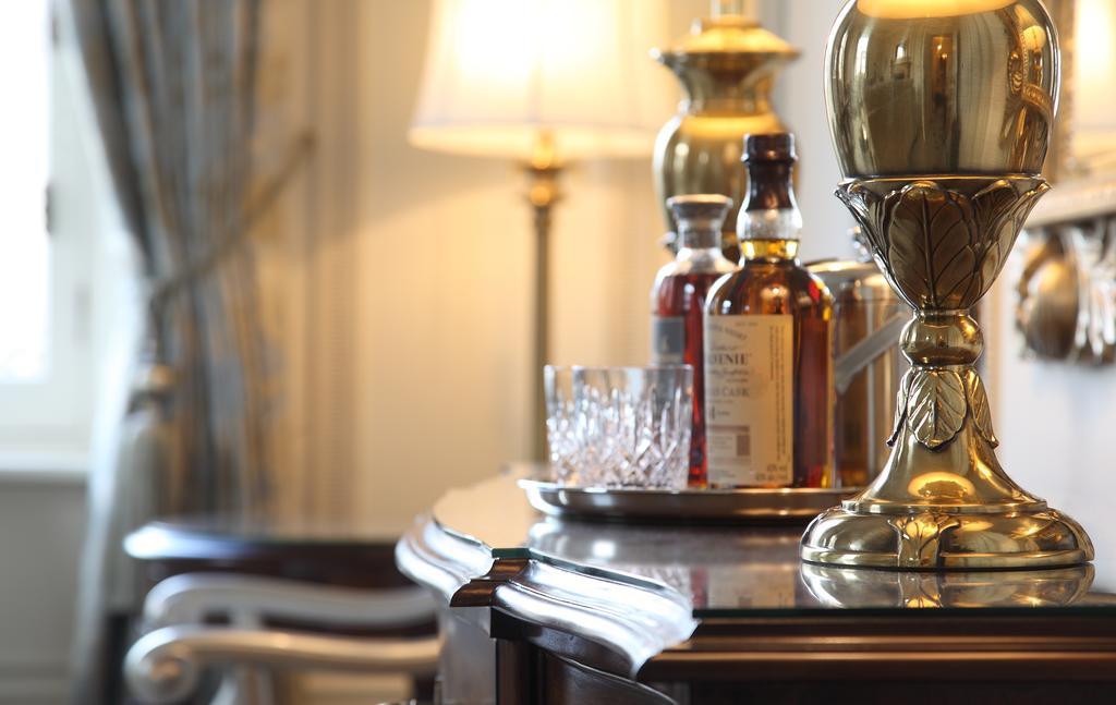 Macdonald Bath Spa Hotel Eksteriør bilde The photo features an elegant interior scene that includes a polished wooden bar or table. On the surface, there are several bottles of liquor, likely whiskey, each with a distinctive label. A glass, possibly for drinking, is positioned near the bott